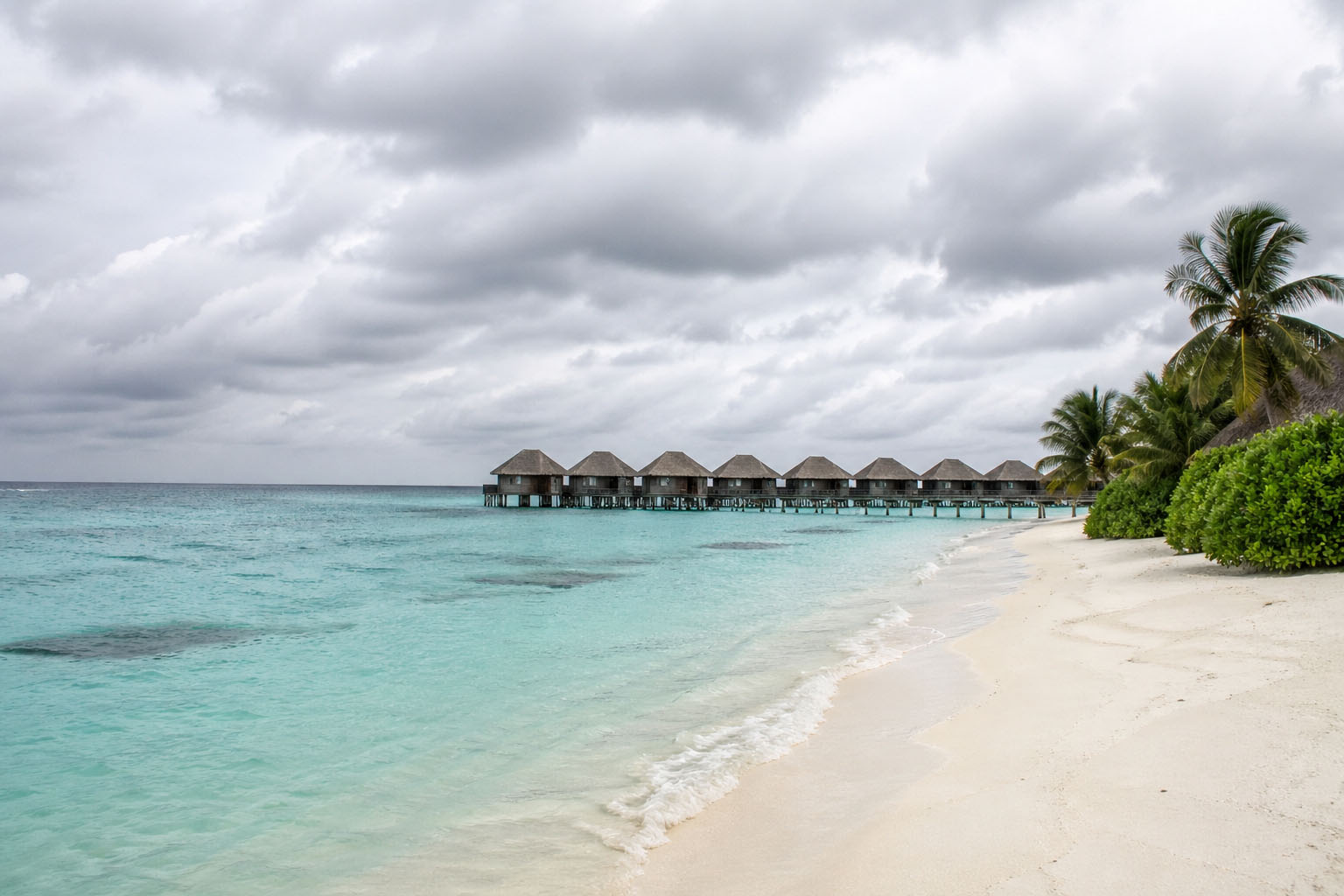 Maldives island beach with overwater villas in October cloudy sky